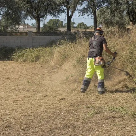 Operario con desbrozadora despejando la hierba seca de una parcela
